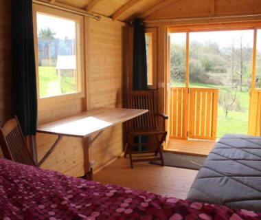 Intérieur de cabine en bois avec lit canapé et porte-fenêtre sur terrasse aux Insolites de la Tellerie