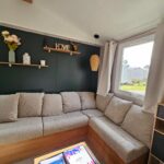 Séjour avec canapé d'angle et étagère décorative près de la fenêtre du Jolie Mobil home 2 chambres (198)