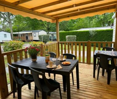 Terrasse couverte avec table et chaises et vue sur mobil-homes dans le camping Kélya Lodge
