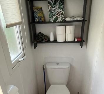 WC avec étagères contenant produits d'entretien et rouleaux de papier dans le camping L éden