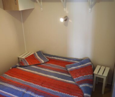 Chambre avec lit double couette rayée et chevet au camping Le Casque Roi