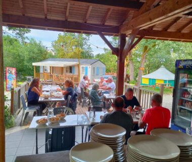 Terrasse couverte avec convives et vaisselle au Fresne cabane insolite du Camping Le Bel Air