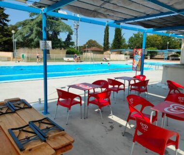 Terrasse ombragée avec chaises rouges et vue sur la piscine à la cabane Le Fresne