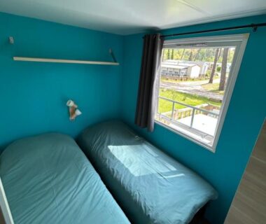 Chambre avec deux lits et fenêtre donnant sur l'extérieur au camping Le Ilô