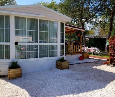 Façade vitrée et terrasse gravillonnée du mobil-home au camping LE PETIT BONHEUR