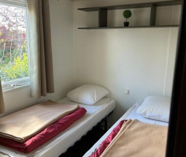 Chambre avec deux lits simples et fenêtre sur jardin au camping Les Pierres Chaudes