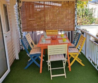Terrasse couverte avec table et chaises multicolores au camping L'Exellence