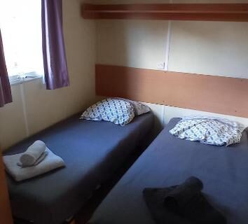 Chambre avec deux lits simples et fenêtre dans le mobil home L'OLIVIER