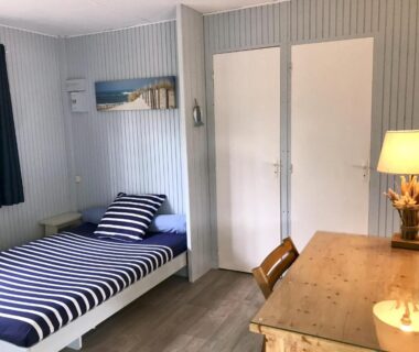 Chambre avec lit rayé et bureau au LOUE JOLI CHALET EN BOIS POUR 2 PERSONNES AU CHM de MONTALIVET