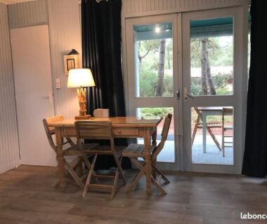 Intérieur avec table, chaises et baie vitrée dans le chalet en bois au CHM de Montalivet