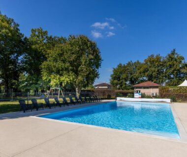 Piscine extérieure bordée de transats et arbres au camping L'Oasis des Dombes