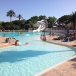 Piscine extérieure avec toboggan et transats bordée de palmiers au camping La Baume 515