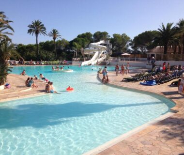 Piscine extérieure avec toboggan et transats bordée de palmiers au camping La Baume 515