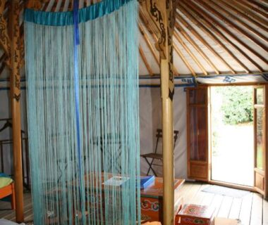 Intérieur de yourte avec lit et rideau de cordelettes dans La Buissonnière Lodges
