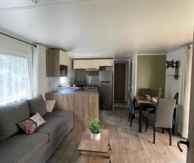 Séjour avec canapé table basse et coin cuisine dans le mobilhome La Carabasse Mobilhome Vias plage