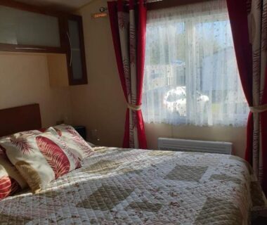 Chambre avec lit double et rideaux dans le mobil-home La Chanterie Agréable Mobil-Home Résidentiel Normand