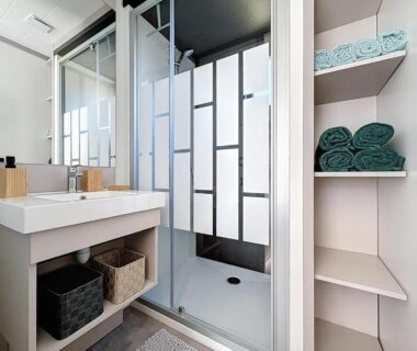 Salle de bain avec douche vitrée vasque et étagères de serviettes dans le camping La Criste Marine