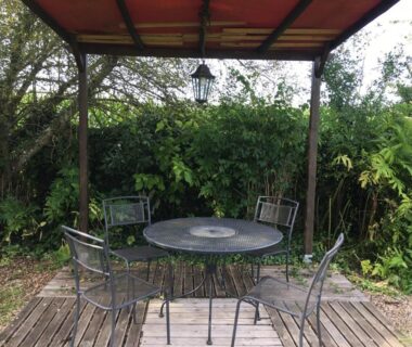 Terrasse en bois couverte avec table ronde et quatre chaises de la roulotte La Dorépontaise