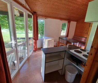 Intérieur de chalet avec kitchenette et baie vitrée donnant sur terrasse au camping La Forêt Enchantée
