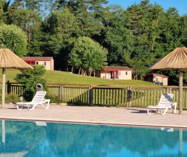 Piscine extérieure avec transats parasols et bungalows en lisière de forêt au camping La Forêt Enchantée