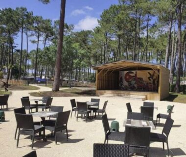 Terrasse extérieure avec tables et scène dans la pinède au camping La Lette fleurie