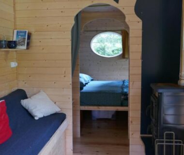 Intérieur de roulotte en bois avec banquette poêle et lit visible à La roulotte aux Nuits Insolites d'Argoumbat