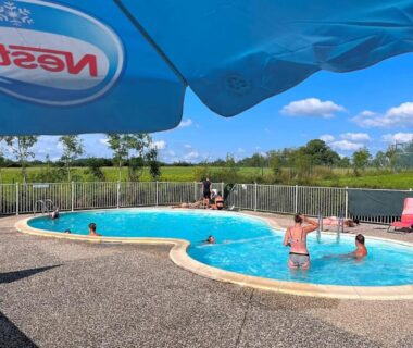 Piscine extérieure avec baigneurs et parasols au camping Le Bruant des Roseaux