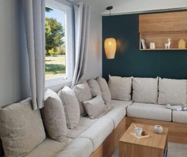 Salon avec canapé d'angle et fenêtre donnant sur jardin dans Le Bungalow du Ferret