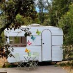 Devant une caravane blanche avec table et chaises au camping Le Cocon au fil de soi