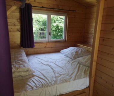 Intérieur en bois avec lit près de la fenêtre dans le chalet Le Domaine du Scorff