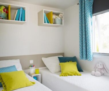 Chambre avec deux lits simples et coussins colorés dans le logement Le Goh Velin