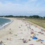 Plage sable avec baigneurs et parasols au camping Le Goh Velin