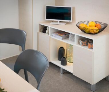 Coin repas avec meuble TV bol de fruits et chaises au camping Le Goh Velin