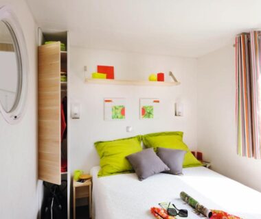 Chambre lumineuse avec lit et coussins verts au camping Le Goh Velin