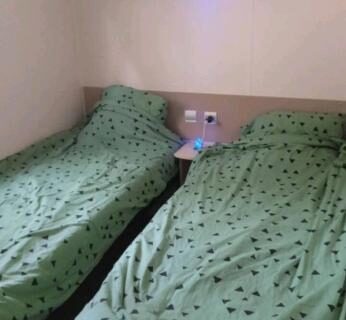 Chambre avec deux lits simples aux couvertures vertes et petite table de chevet au camping Le Kraken