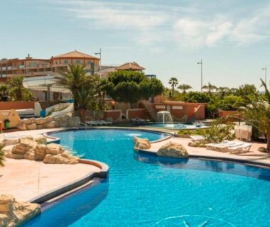 Piscine extérieure bordée de rochers et palmiers au camping Le Lagon Rose nice bungalow Camping SIBLU le Mar Estang