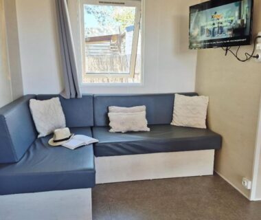 Coin salon avec banquette et télévision dans le Lounge Mobil Home au Camping Les Dunes