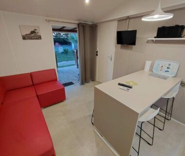 Salon avec canapé rouge dans Le Mobilhome Douillet climatisé 5 pers en camping, proche plage, 2 SDB, 2 WC