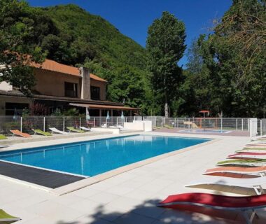 Piscine extérieure avec transats et bâtiment en arrière-plan au camping Le Moulin du Pont D’Aliès