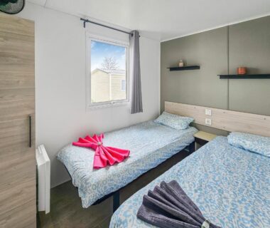 Chambre avec deux lits simples et serviettes pliées près de la fenêtre au camping Le Nocia