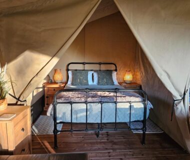 Intérieur de tente avec lit en fer et tables de chevet dans Le Ranch Camping et Glamping