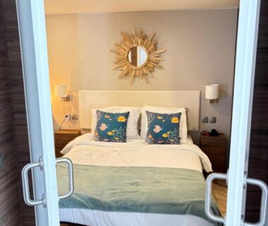Chambre avec lit double coussins décoratifs et miroir soleil au camping Le Cabanon