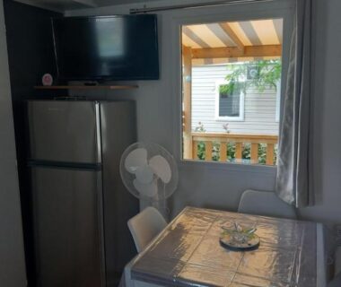 Intérieur du mobil home avec table réfrigérateur et télévision au camping L'échapée verte