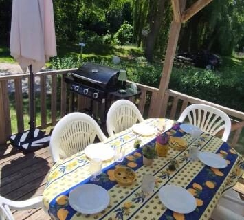 Terrasse en bois avec table chaises et barbecue au camping L'échappée verte au bord de l'Eure