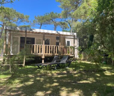 Mobil-home sur terrasse en bois avec transats dans espace ombragé au camping L'écureuil