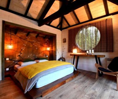 Intérieur de chambre en bois avec lit double et fenêtre ronde dans le camping Les 7 Montagnes