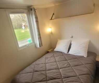 Intérieur du mobil-home avec lit double et fenêtre donnant sur le parc au camping Les Berges Du Cele