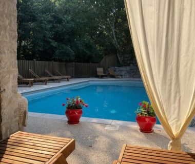 Coin piscine avec chaises longues et pots rouges fleuris au camping Les Chalets de Labeaume