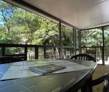 Terrasse couverte avec table et chaises au milieu des arbres du camping Les Chalets de Labeaume