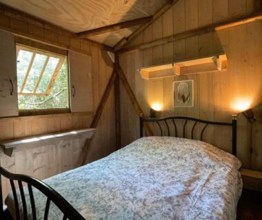 Intérieur de chalet en bois avec lit et fenêtre dans Les Chalets de Labeaume